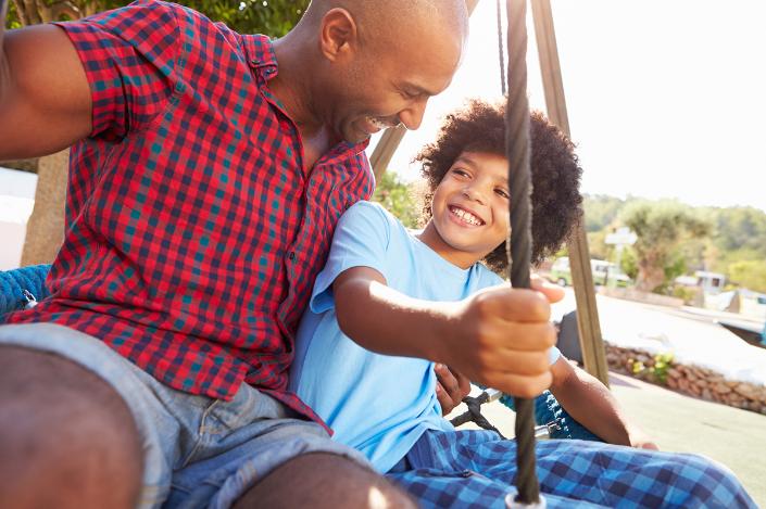 Man and child sitting on tree swing